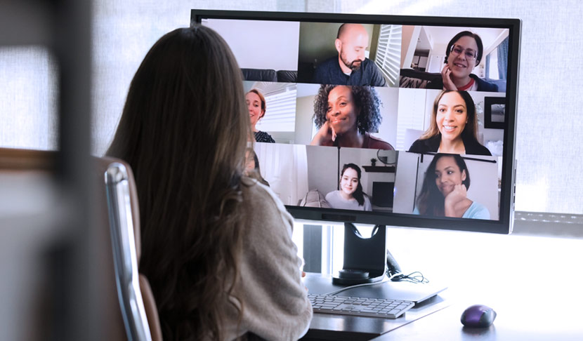 Das Bild zeigt eine Frau mit langen dunklen Haaren, die vor einem Bildschirm bei einer Videokonferenz sitzt